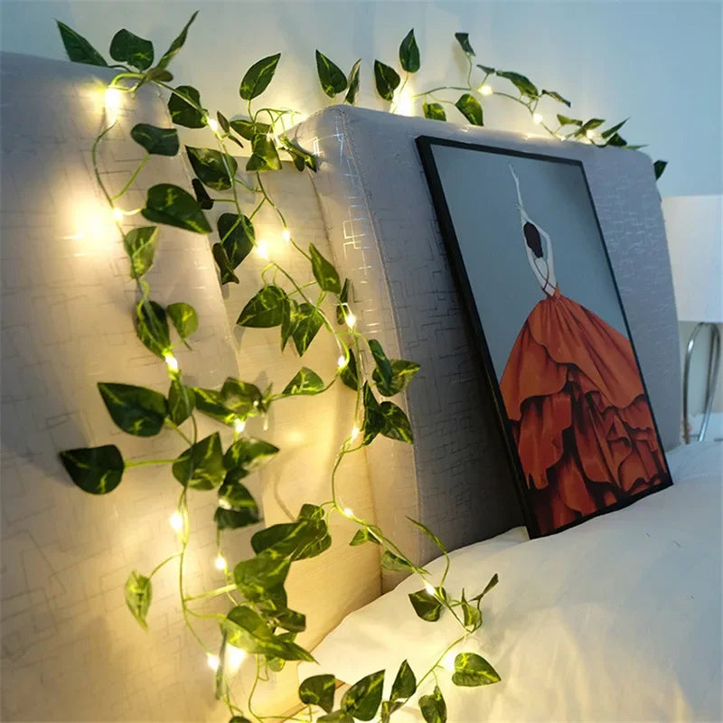 Ivy fairy lights draped elegantly over a bed headboard, softly illuminating a framed artwork with a warm, ambient glow.