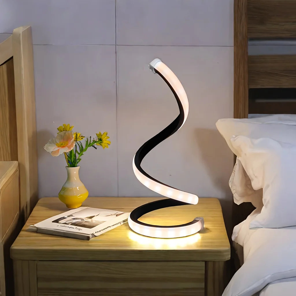 Modern spiral LED lamp in matte black, emitting a soft warm glow on a bedside table beside a book and a vase with yellow flowers, creating a cozy and elegant nighttime atmosphere, ThuisGemak.