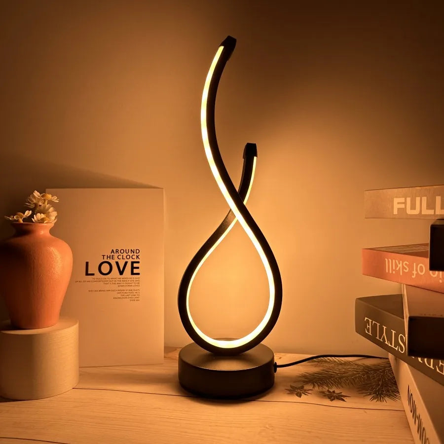 Modern spiral LED table lamp in matte black, emitting a soft amber glow on a wooden surface surrounded by books and minimalist decor, creating a serene evening ambiance, ThuisGemak.