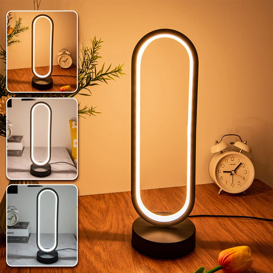 Modern oval-shaped LED lamp in matte black, emitting a warm ambient glow on a wooden surface beside a minimalist clock and decor, creating a cozy and contemporary atmosphere, ThuisGemak.