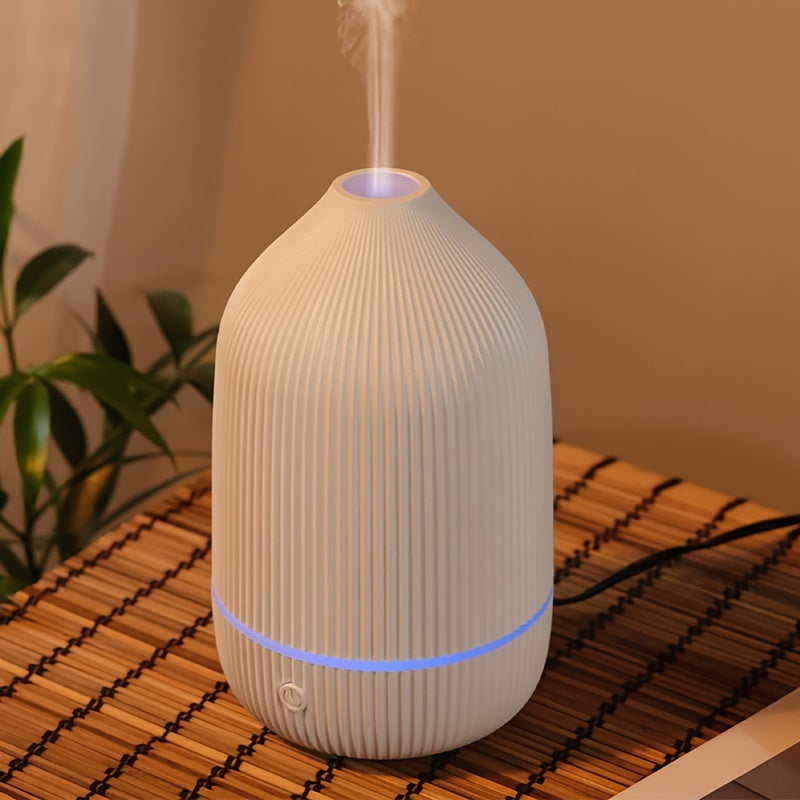 A minimalist white aroma diffuser with a soft blue LED glow placed on a bamboo mat in a cozy living room setting.